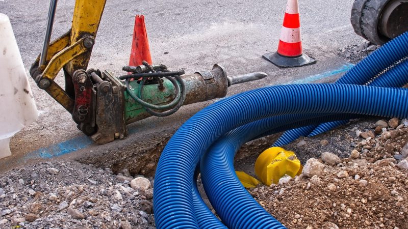 Construction site, road work. Hydraulic crushing hammer. Plastic pipes for electric cables.