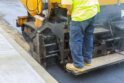 Workers making asphalt with shovels at road construction paving a road